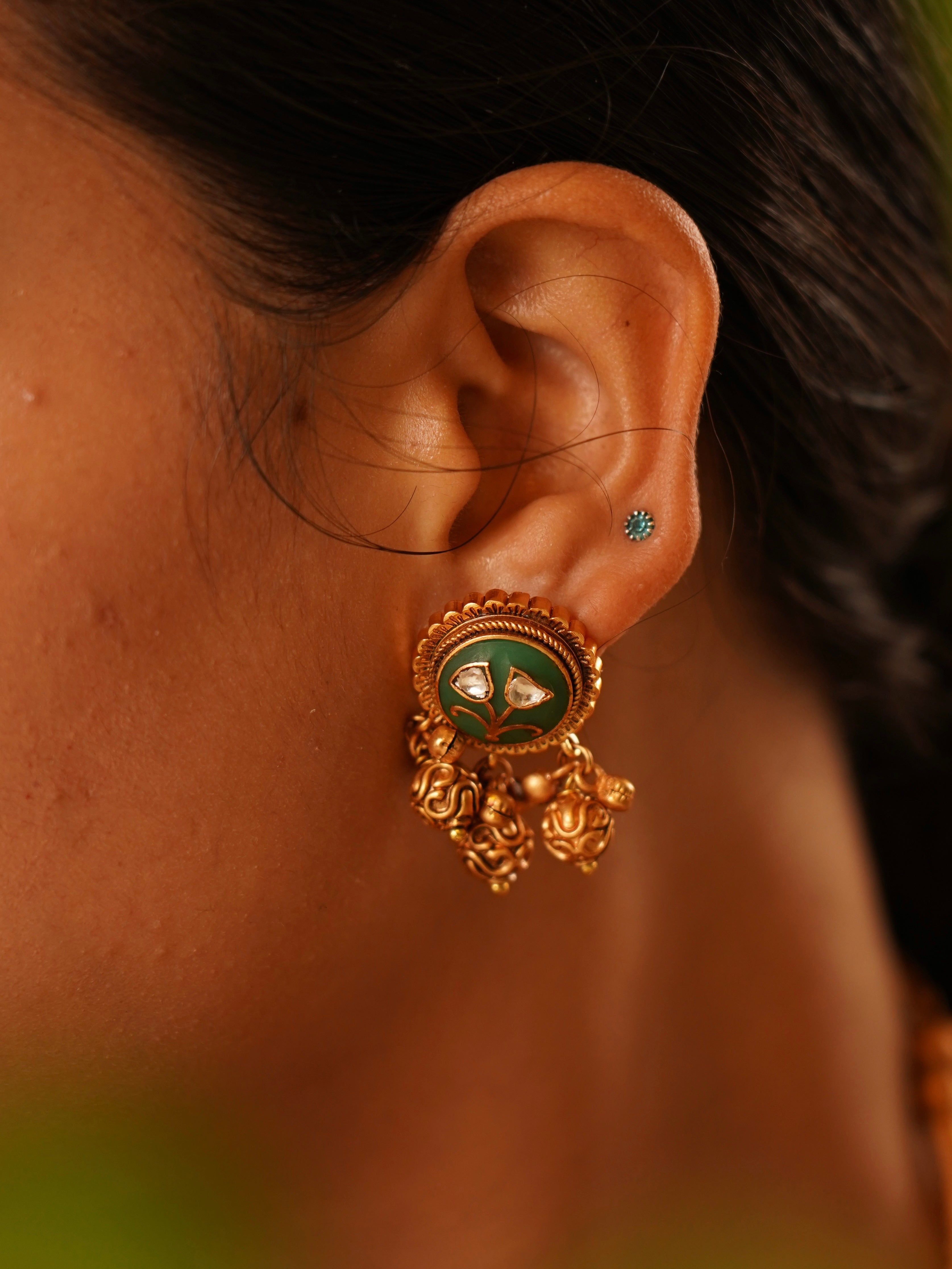 Side view of gold hasli necklace featuring green enamel and dangling details